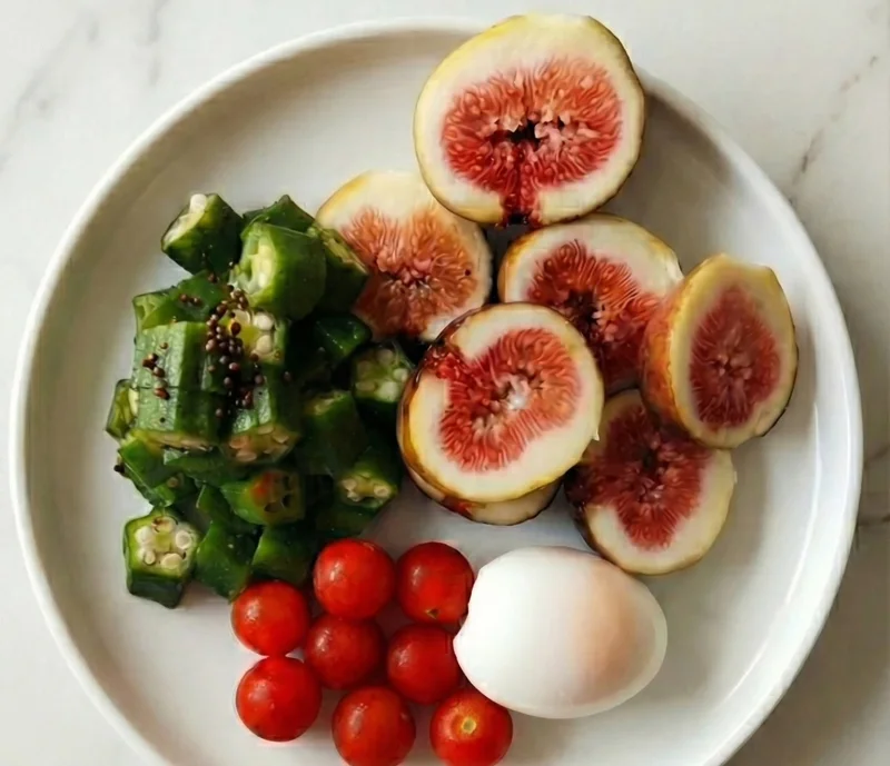 Light plate with sliced figs, okra, cherry tomatoes and a soft-boiled egg